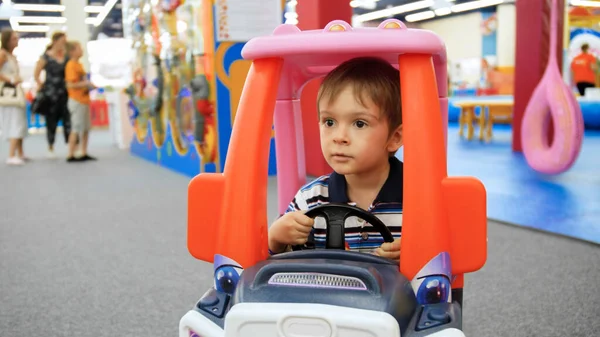 Retrato de menino dirigindo brinquedo carro de plástico no playground no shopping — Fotografia de Stock