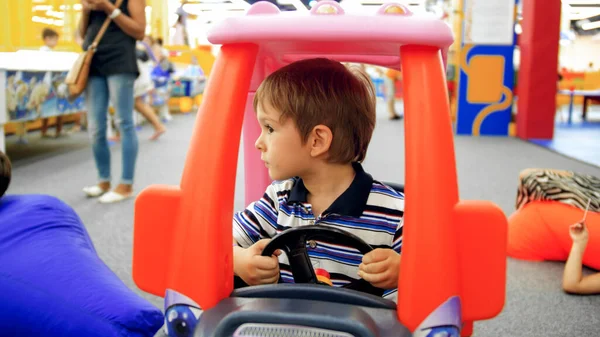 Retrato de menino sorridente dirigindo carro de brinquedo na sala de jogos no shopping — Fotografia de Stock