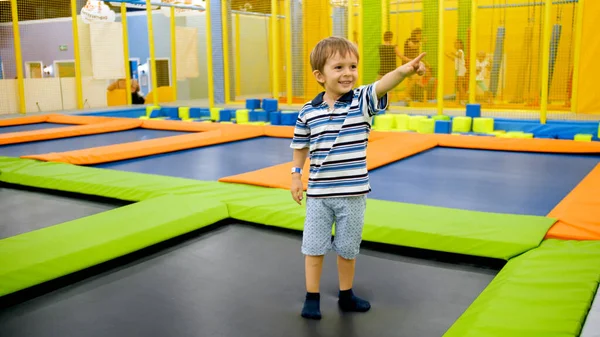 Retrato de menino sorridente feliz se divertindo em trampolins e apontando com o dedo . — Fotografia de Stock