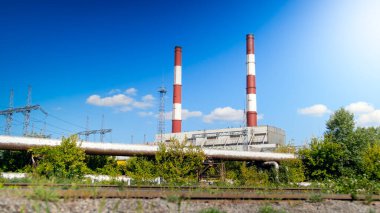 Açık mavi gökyüzüne karşı elektrik santralindeki iki kırmızı ve beyaz bacanın görüntüsü