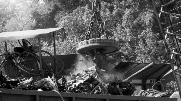 Black and white image of big industrial electric magnet sorting metal scrap on the junkyard — Stock Photo, Image