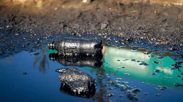 Фотография пластиковой бутылки, лежащей на грязной земле, загрязненной нефтью и токсичными отходами. Концепция вреда окружающей среде и экологии — стоковое фото