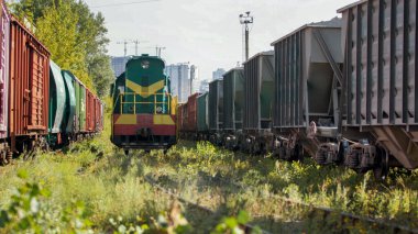 Eski dizel trenin görüntüsü ve uzun sıra kargo trenleri ve vagonlar traktör merkezinde.