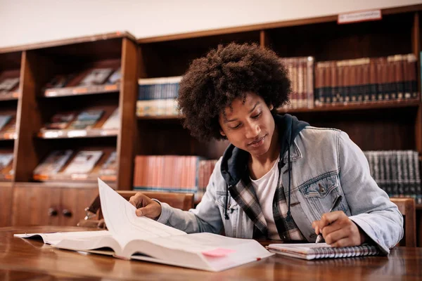 Student making notes from books in library — Stock Photo, Image