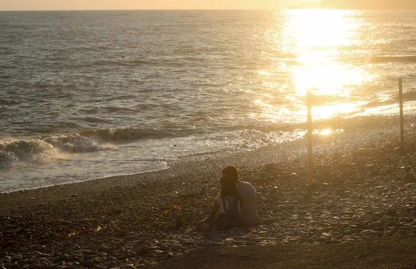 People on the seafront, a couple of people sitting on the coast, sunset on the sea, loving people, the rest of the sea, people on the beach — Stock Photo, Image