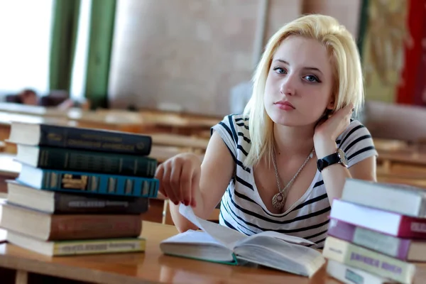 Schattige blonde lezen van een boek, zittend op Bureau in de klas — Stockfoto