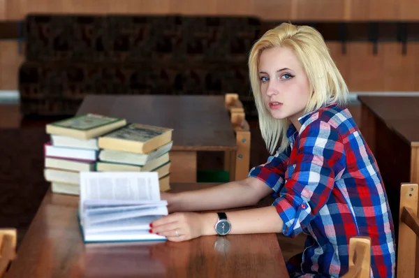 Jonge blonde meisje in een plaid shirt zit op Bureau, houden een open boek — Stockfoto