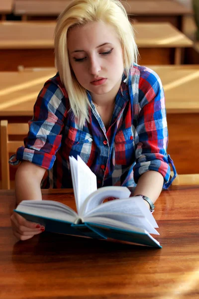 Jonge blonde in een plaid shirt zitten aan de balie in de klas, boek te houden — Stockfoto