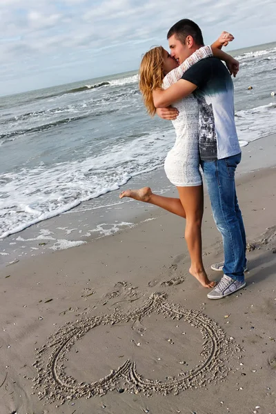 Young couple embracing by the sea or ocean. On the sand pattern in the form of heart — Stock Photo, Image
