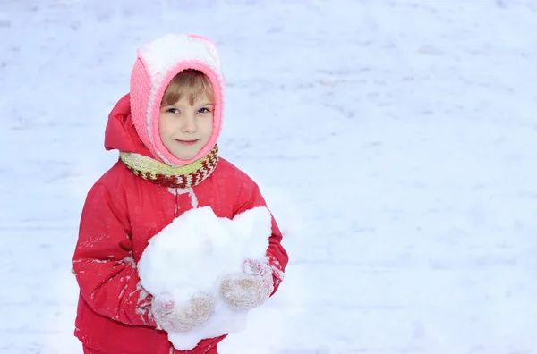 Ett barn ser in i kameran, snö, i hans händer en snöboll, mot en bakgrund av vita snön — Stockfoto