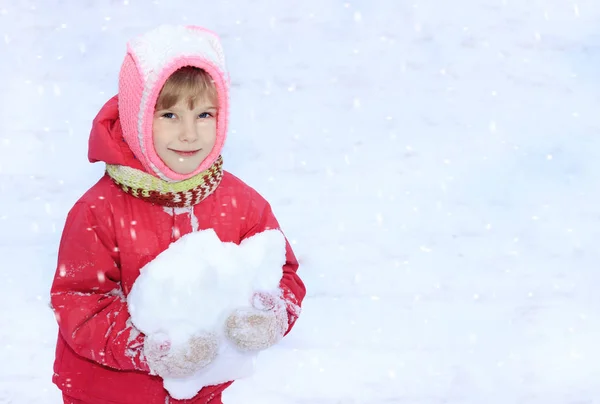 A child looks into the camera, snow, in his hands a snowball, against a background of white snow — Stock Photo, Image