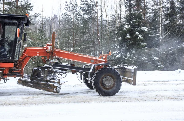 Winter. Snowing. The tractor clears the snow from the road.