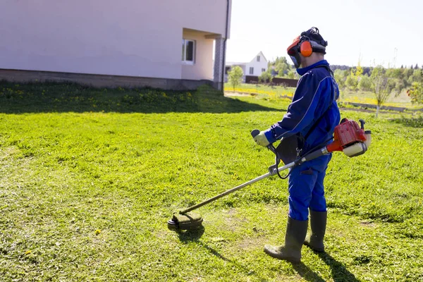 Um homem de fato azul. Em um capacete protetor e fones de ouvido. Produz ervas de colheita. O rosto não se concentra — Fotografia de Stock