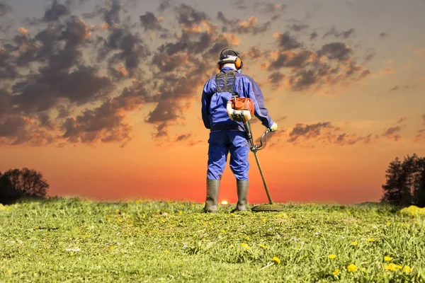 Un hombre con un traje azul. En un casco protector y auriculares. Produce la cosecha de hierbas. La cara no se enfoca — Foto de Stock