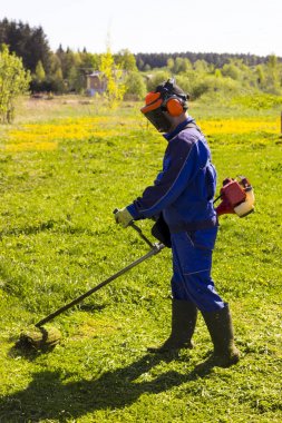 Mavi elbiseli bir adam. Koruyucu bir kask ve kulaklık. Otlar hasat üretir. Yüz odaklanmak değil