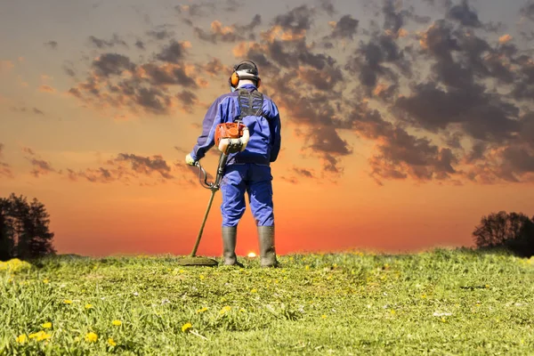 Un hombre con un traje azul. En un casco protector y auriculares. Produce la cosecha de hierbas. La cara no se enfoca — Foto de Stock