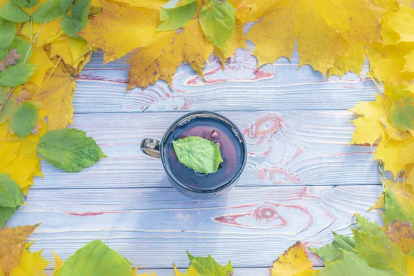 Fondo de madera. hojas amarillas alrededor. en el centro hay una taza de té en ella es una hoja de un árbol — Foto de stock gratuita