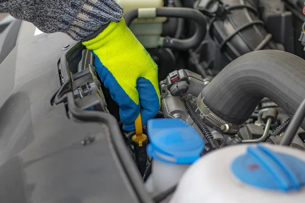 Een mannelijke hand in een gele handschoen houdt het deksel vast. controle van het oliepeil — Stockfoto