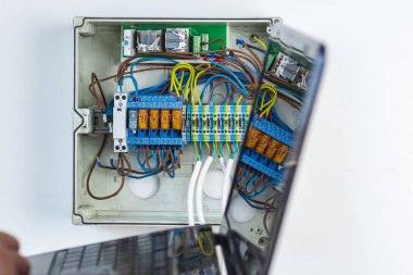 Büyücü akıllı ev kontrolünü bir bilgisayar aracılığıyla kuruyor. Elinde bir dizüstü bilgisayar var. Otomatik ve röleli arka plan kalkanı. çok kablo.