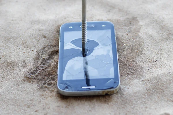 Smartphone se encuentra en la arena. un clavo es clavado en él. primer plano . —  Fotos de Stock