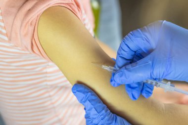 Yakın plan. Mavi eldivenli doktor iğne yapıyor. Bebeğim, elin iğneye hazır olmak üzere..