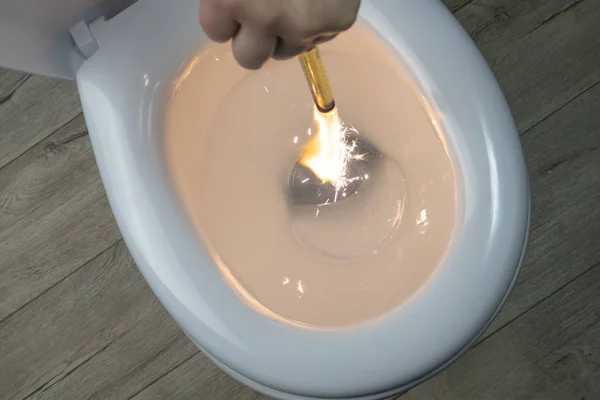 White toilet bowl on a wooden background. the hand lowers the lit firecracker. close-up. — Stock Photo, Image