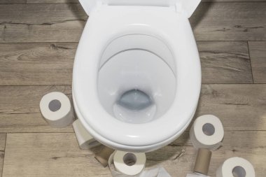 Ahşap zemindeki beyaz tuvalet eski moda. Etrafında bir sürü tuvalet kağıdı var..