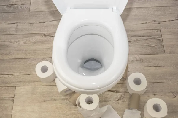 WC bianco su un pavimento in legno in stile retrò. ci sono molti rotoli di carta igienica intorno ad esso . — Foto Stock