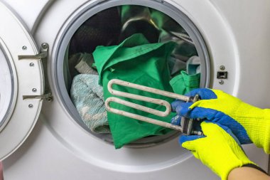 Çamaşır makinesi bozuldu. Usta zemin kısmını geri alır. Bir spiral ve ayarlanabilir anahtarın ellerinde. Yakın plan.