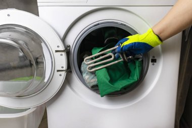 Çamaşır makinesi bozuldu. Usta zemin kısmını geri alır. Bir spiral ve ayarlanabilir anahtarın ellerinde. Yakın plan.