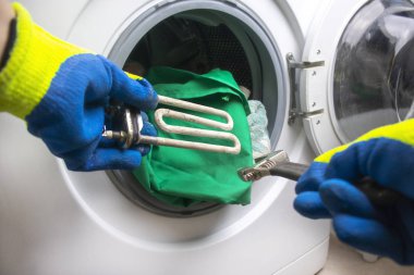 Çamaşır makinesi bozuldu. Usta zemin kısmını geri alır. Bir spiral ve ayarlanabilir anahtarın ellerinde. Yakın plan.