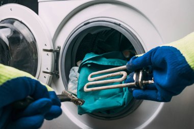 Çamaşır makinesi bozuldu. Usta zemin kısmını geri alır. Bir spiral ve ayarlanabilir anahtarın ellerinde. Yakın plan.