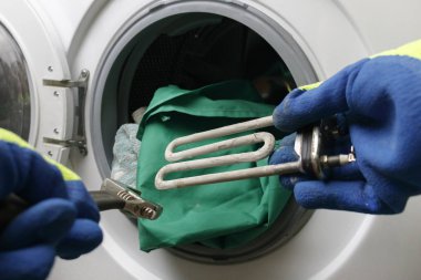 Çamaşır makinesi bozuldu. Usta zemin kısmını geri alır. Bir spiral ve ayarlanabilir anahtarın ellerinde. Yakın plan.