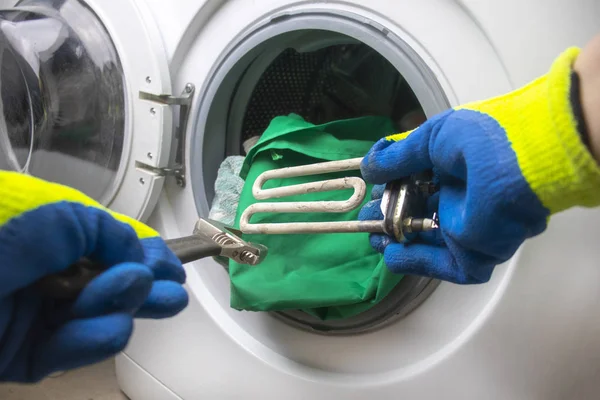 Afbraak wasmachine. De meester haalt het vloerdeel op. In de handen van een spiraalvormige en verstelbare sleutel. Close-up — Stockfoto