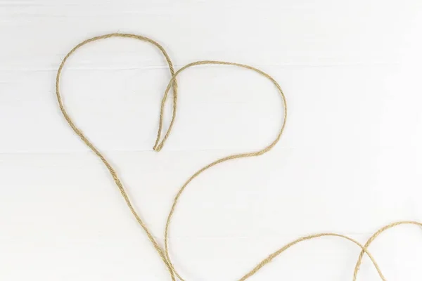 Šedé lano leží ve tvaru srdce. Dřevěné pozadí v bílé — Stock fotografie