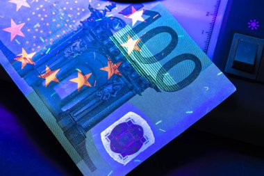 100 Euro banknot. Banknotların orijinalliğini doğrulamak için ultraviyole ışıkta yatıyordu. Yakın plan.
