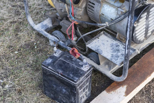 接近中だ街路灯だ電流を発生させるガソリン発電機。充電のために車のバッテリーが接続されています。バックアップまたは非常用電源。発電機は新しいものじゃない — ストック写真