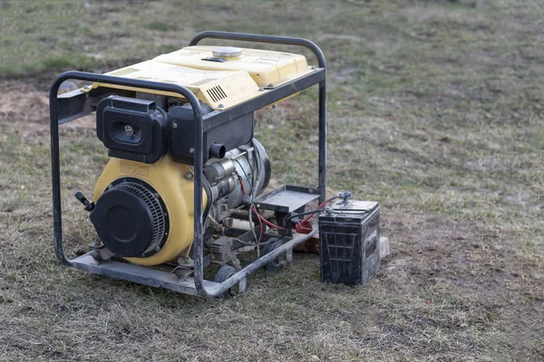 close-up. Street lighting. A gasoline-powered generator that produces current. A car battery is connected for charging. Backup or emergency power source. The generator is not new