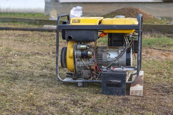 Primer plano. alumbrado público. Un generador de gasolina que produce corriente. Una batería de coche está conectada para cargar. Fuente de energía de emergencia o respaldo. El generador no es nuevo — Foto de Stock