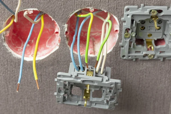 3 boxes of red color. Wall mounted. Of them stick out wires of different colors. one has a power outlet. Green, white, blue. Close-up. — Stock Photo, Image