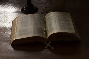 Ahşap işlemeli cam masa. Bu konuda bir kitap var. İçinde bir haç var. Loş ışık. Karanlık. Rengi var.