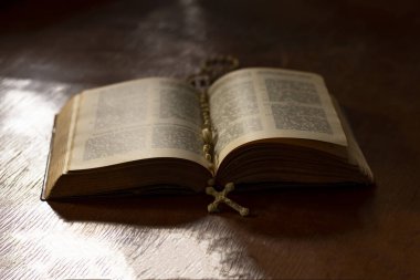 Ahşap işlemeli cam masa. Bu konuda bir kitap var. İçinde bir haç var. Loş ışık. Karanlık. Rengi var.