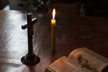 Ahşap işlemeli cam masa. Bu konuda bir kitap var. Üzerinde bir haç var, bir mum yanıyor. Loş ışık. Karanlık. Rengi var.