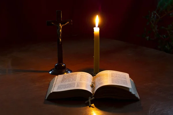 Drewniany witrażowy stół. Jest o tym książka. Na nim krzyż, świeca płonie. Przyciemnione światło. Ciemność. Jest odcień. — Zdjęcie stockowe