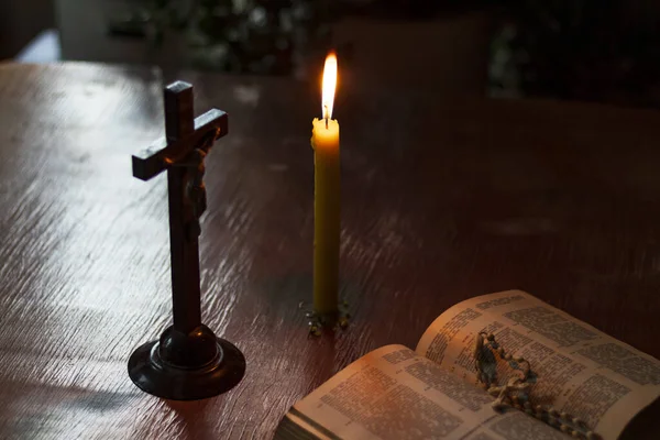 Mesa de vidrio manchado de madera. Hay un libro en él. en ella hay una cruz, una vela está ardiendo. Luz tenue. Oscuridad. Hay un tinte —  Fotos de Stock