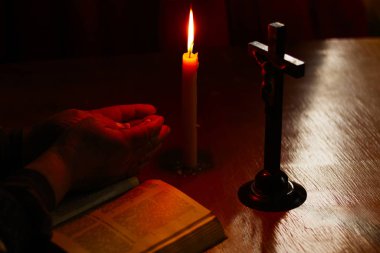 Tahta masa eski usul. Üzerinde bir mum ve bir haç var. Yaşlı bir kadının elleri kitaptan üstündür. Avuçlar katlandı