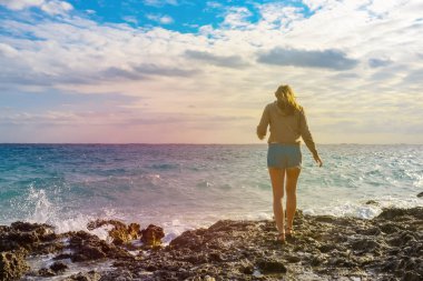 Okyanus. Yaz. Kot pantolonlu bir kız sırtı bize dönük olarak sahile gidiyor. Boşluğu kopyala.