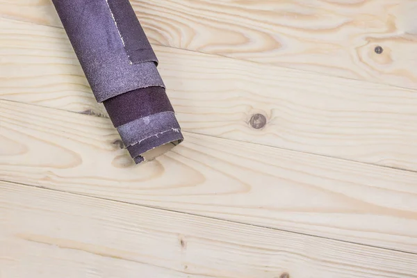 Papel de lija retorcido en un rollo se encuentra en una tabla de madera. Primer plano. Hay un tinte . — Foto de Stock