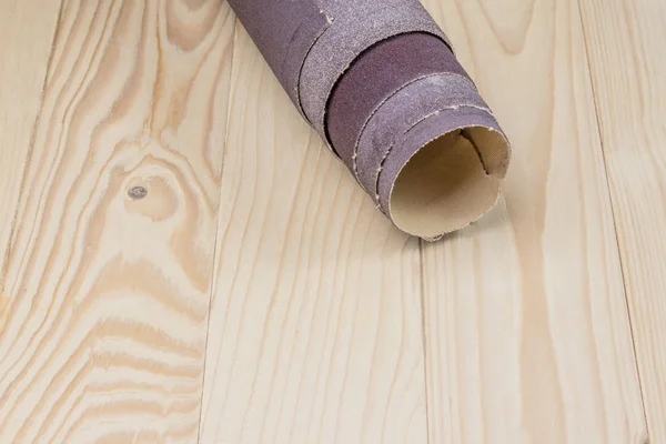 Písečný papír zkroucený do role leží na dřevěné desce. Detailní záběr. Je tu odstín.. — Stock fotografie
