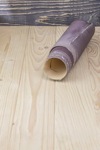 Papel de lija retorcido en un rollo se encuentra en una tabla de madera. Primer plano. Hay un tinte . —  Fotos de Stock